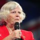 Ann Widdecombe wears a red jacket and holds a microphone while speaking at the Reform Party 2024 Conference.