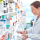Pharmacist standing in front of shelves in pharmacy, holding medicine boxes in hands.