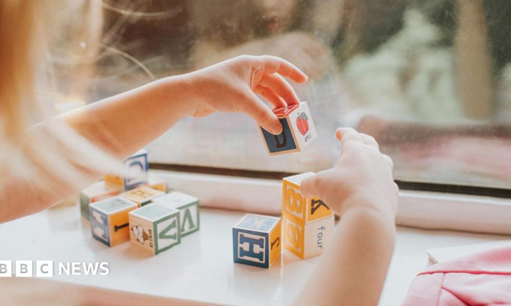 A child plays with letter blocks in front of a window