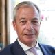 Nigel Farage sitting in a pub while wearing a white shirt and navy blazer. He is smiling.