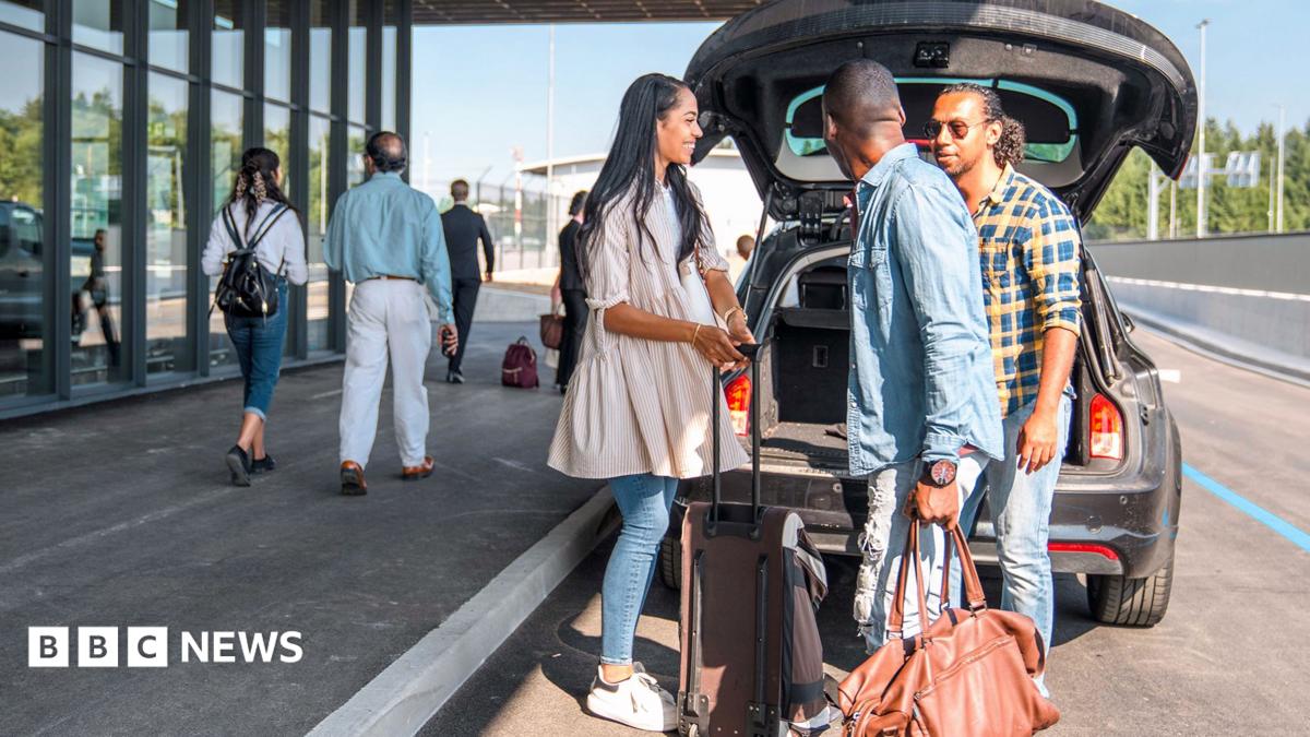 A sign outside Gatwick airport reads 'check-in & bag drop; north terminal Gatwick', while people walk past wheeling baggage along the concrete floor, image taken in 2024.