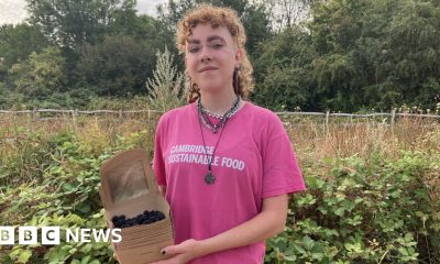 Alex Vardill wearing a pink T-shirt, smiling straight at the camera and holding a box of blackberries.