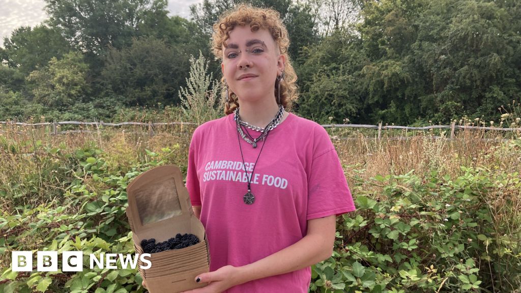 Alex Vardill wearing a pink T-shirt, smiling straight at the camera and holding a box of blackberries.