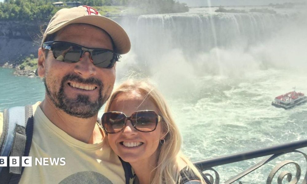 Man and woman wearing sunglasses smiling in front of a waterfall