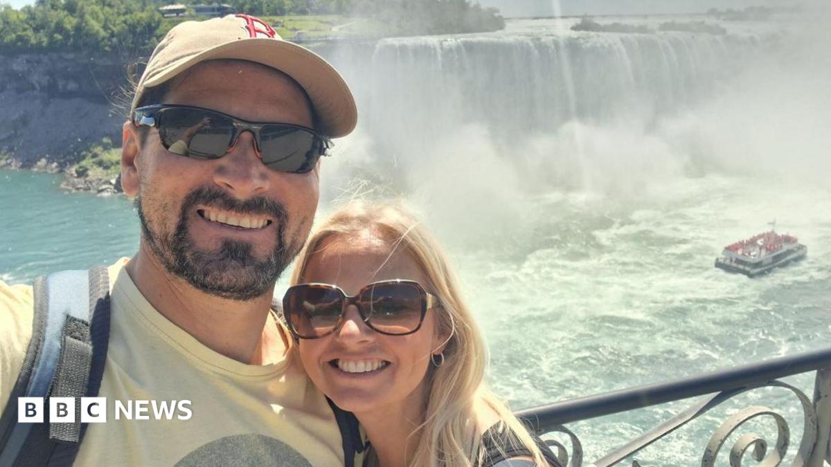 Man and woman wearing sunglasses smiling in front of a waterfall