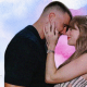 Travis Kelce and Taylor Swift embrace each other in a designed image with a blue and pink background.