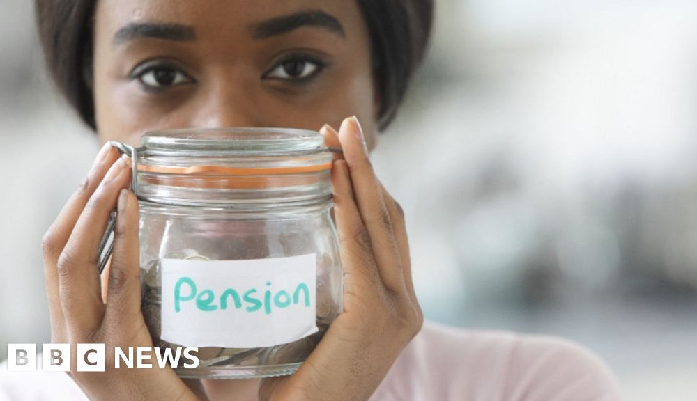 A young woman with dark hair holds up glass jar of coins labelled 'pension'.