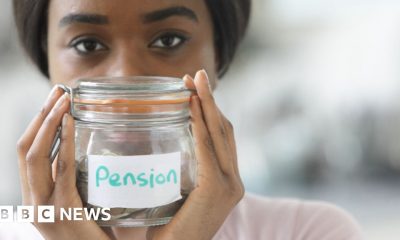 A young woman with dark hair holds up glass jar of coins labelled 'pension'.