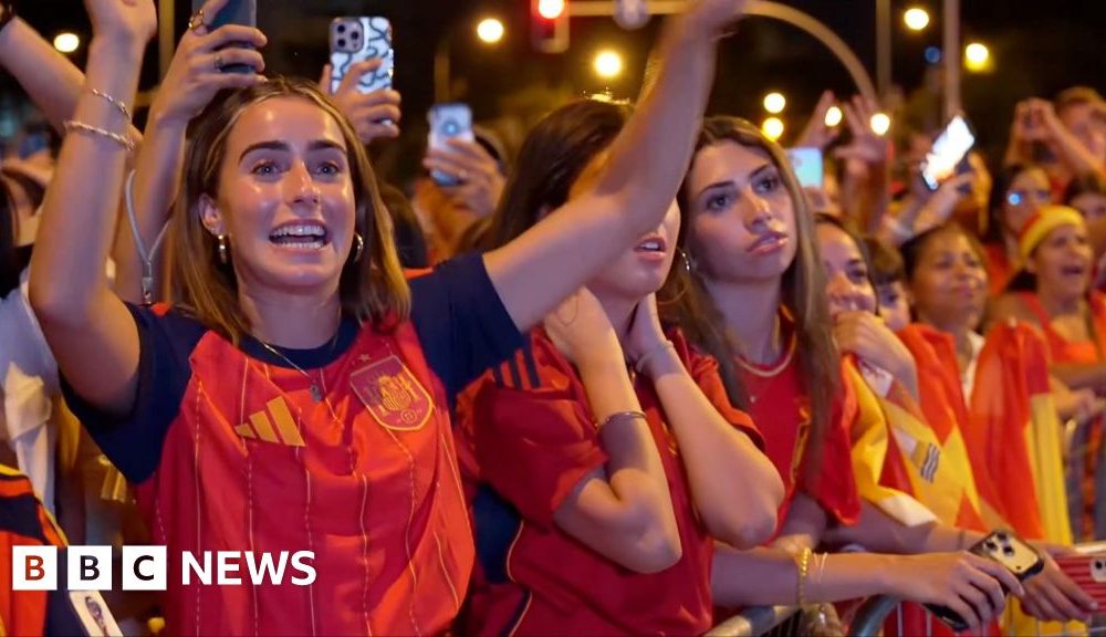A female celebrates her country's World Cup win with her hands raised in a crowd full of Spanish supporters.