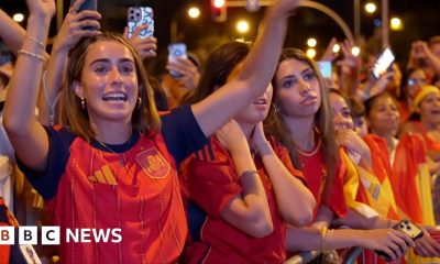 A female celebrates her country's World Cup win with her hands raised in a crowd full of Spanish supporters.