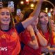 A female celebrates her country's World Cup win with her hands raised in a crowd full of Spanish supporters.