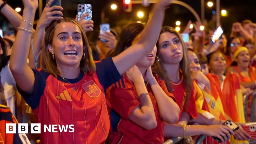 A female celebrates her country's World Cup win with her hands raised in a crowd full of Spanish supporters.