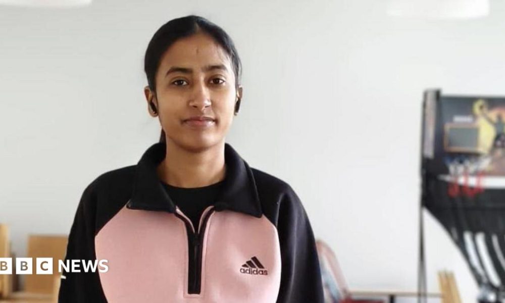 A young woman in a pink and black top stands next to a table tennis table.