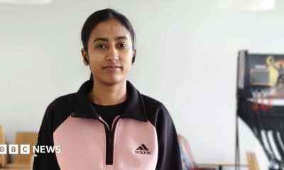 A young woman in a pink and black top stands next to a table tennis table.
