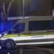 A white Garda van with a yellow stripe along its side pulls out onto a main road on a dark night.