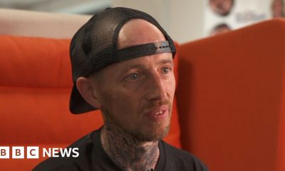 Steven, a man in a black t shirt and black snapback cap sat on a large orange chair.  He has a short red haired goatee.