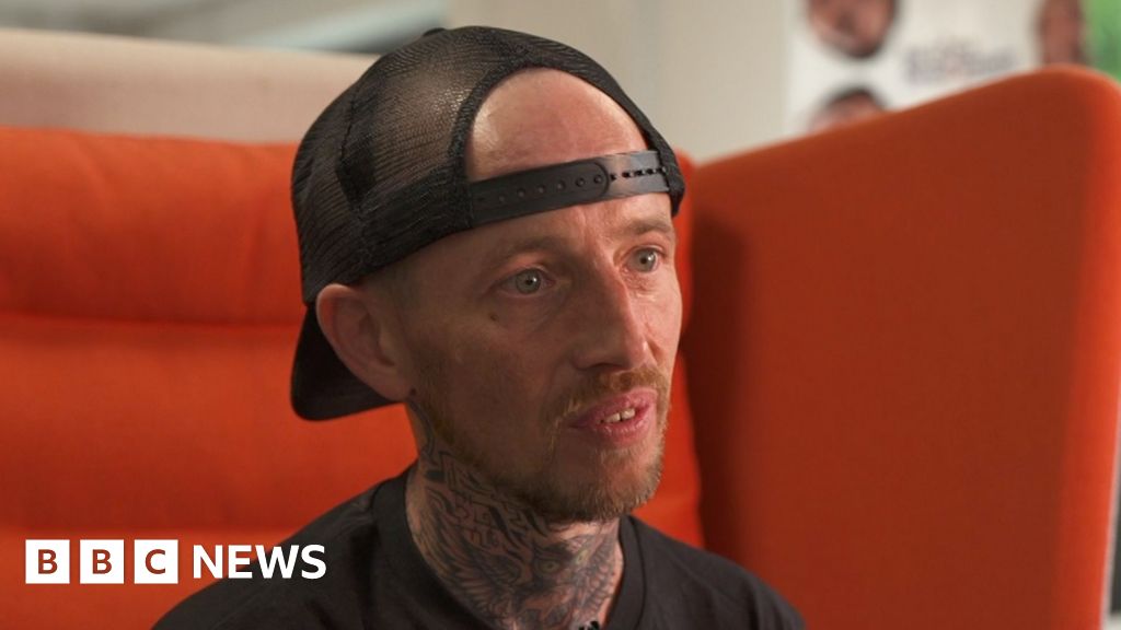 Steven, a man in a black t shirt and black snapback cap sat on a large orange chair.  He has a short red haired goatee.