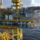 Offshore oil and gas platform marked “JACKDAW 30/2a” standing on yellow support legs above the sea, with industrial equipment, pipework and a crane visible under a partly cloudy sky.