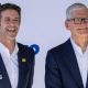 Apple's incoming chief executive John Ternus standing next to his predecessor Tim Cook. Both are smiling for cameras at an Apple event and wearing an almost identical blue blazer and white collared shirt.