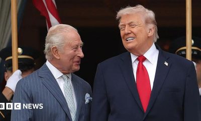 King Charles looking at Donald Trump, both wearing suits and smiling.