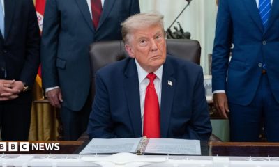 US President Donald Trump sitting in the White House wearing a blue suit jacket, white shirt and red tie.
