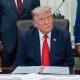 US President Donald Trump sitting in the White House wearing a blue suit jacket, white shirt and red tie.