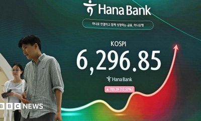 A man and a woman walk past an electronic screen showing 31 July's Kospi trading figures