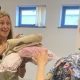 A woman holding a number of items that look like blankets, with a woman handing them to her. They both have long hair.