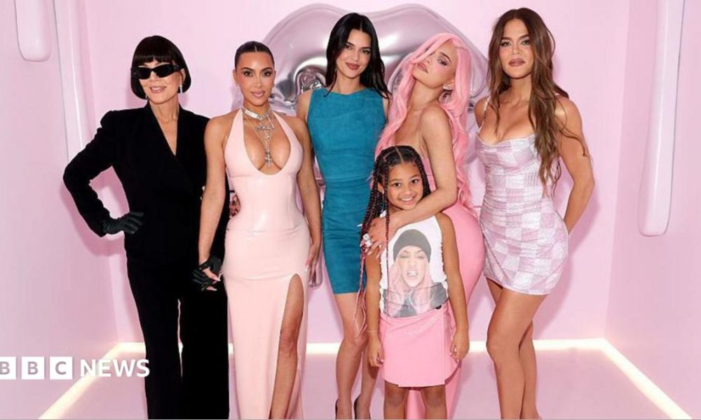 The Kardashian family is pictured posing in front of a pink background