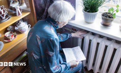 A stock image of an elderly woman holding an energy bill while sat close to a radiator.