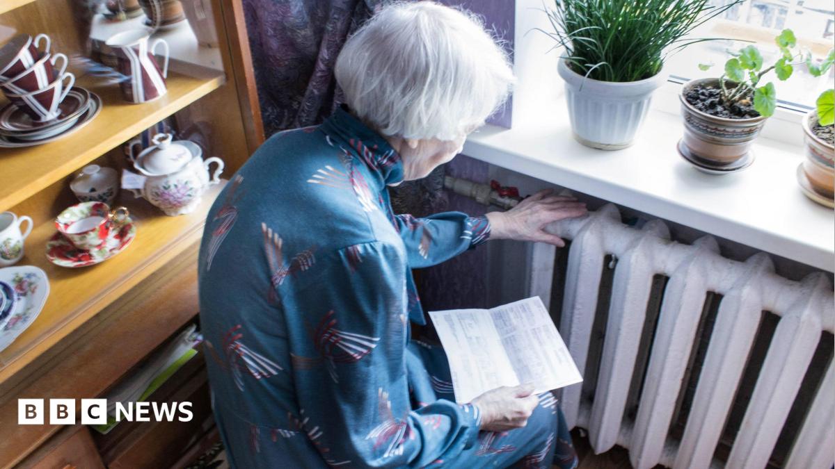 A stock image of an elderly woman holding an energy bill while sat close to a radiator.
