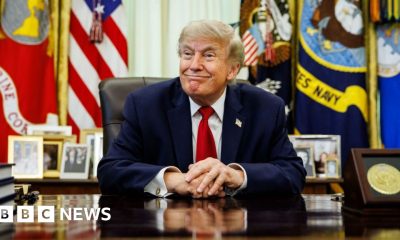 US President Donald Trump smiles while sitting at the Resolute Desk