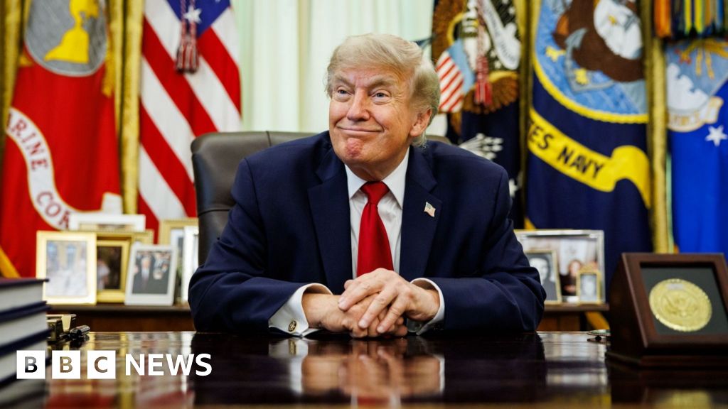 US President Donald Trump smiles while sitting at the Resolute Desk