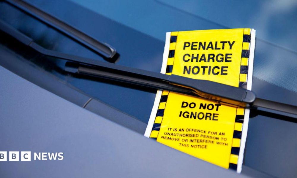A bright yellow ticket under a car windscreen wiper reads "penalty charge notice do not ignore: it is an offence for an unauthorised person to remove or interfere with this notice".