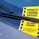 A bright yellow ticket under a car windscreen wiper reads "penalty charge notice do not ignore: it is an offence for an unauthorised person to remove or interfere with this notice".