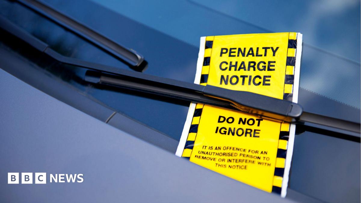 A bright yellow ticket under a car windscreen wiper reads "penalty charge notice do not ignore: it is an offence for an unauthorised person to remove or interfere with this notice".