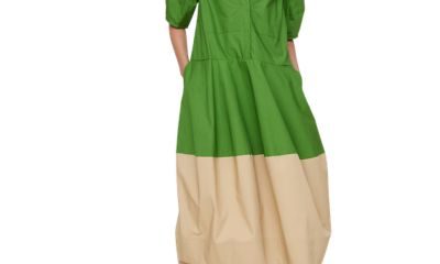 A woman wearing a colorblock dress that is green and beige, as well as brown sandals, a red beaded necklace, and gold earrings