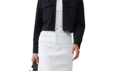 A woman wearing a black blazer, white top, white skirt, and carrying a black handbag