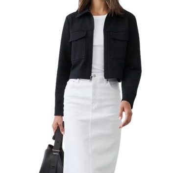 A woman wearing a black blazer, white top, white skirt, and carrying a black handbag