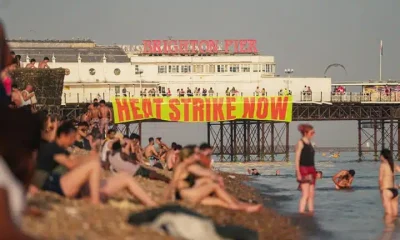 A banner hanging from Brighton pier reads Heat Strike Now as campaigners demand maximum working temperature