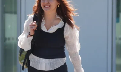 Ellie Kamio, one of the Filton 25, smiling while walking outside Woolwich Crown Court, London, in April 2026 with one hand on her shoulder keeping her backpack strap in place