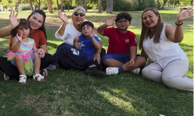A family with young children wave and smile while sat on grass as part of a news report on Spain's approach to immigration in October 2025