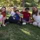 A family with young children wave and smile while sat on grass as part of a news report on Spain's approach to immigration in October 2025