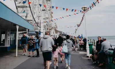 A bustling scene at Llandudno promenade in Wales with people walking near a Ferris wheel adorned with flags. Days out like this will not be affordable for many UK families due to money worries.