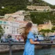 Side view of smiling female tourist with long hair exploring Amalfi Coast and walking the authentic streets with colourful houses by the sea