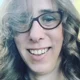 Close up selfie of Heather Herbert, who wears cat eye shaped glasses and has bouncy curls in her hair, and made mean comments online about Ann Widdecombe dying