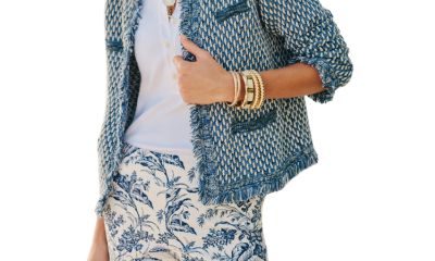 A woman wearing a blue/cream knit cardigan, a white top, blue-and-white floral print pants, and several jewelry pieces