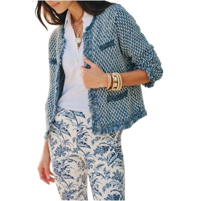 A woman wearing a blue/cream knit cardigan, a white top, blue-and-white floral print pants, and several jewelry pieces