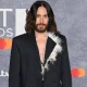 Jared Leto in a suit blazer with his bare chest exposed at the top, posing infront of Brit Award backdrop. Year unknown.