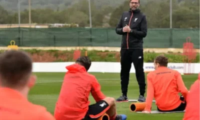 Jürgen Klopp stands to address his football players, who are sat with their backs to camera all wearing the same red jacket, during what he describes as a ‘pre-season training’ camp in La Manga in February 2017